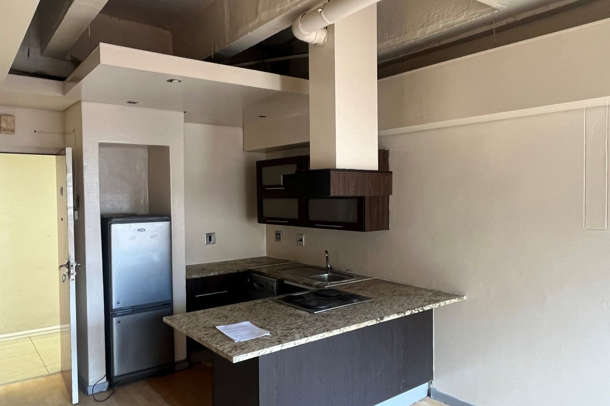 Compact kitchen featuring granite countertops, dark cabinetry, a built-in hob, and an integrated extractor fan, set within an open-plan living space.