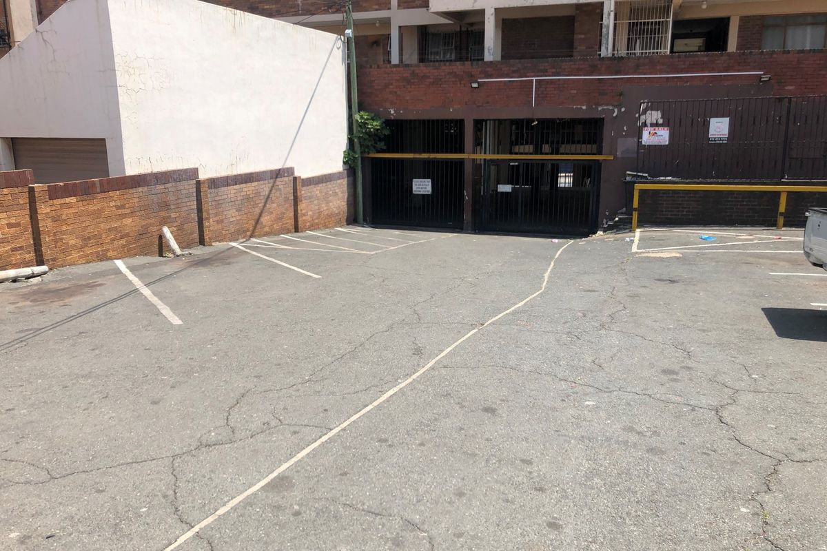 Exterior view of a paved parking area with access to a secure garage facility featuring brick boundary walls and security gates.