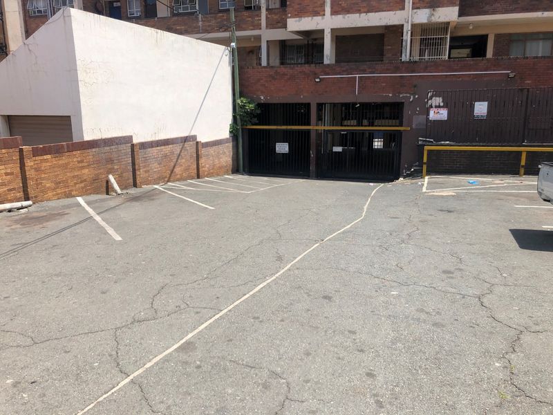 Exterior view of a paved parking area with access to a secure garage facility featuring brick boundary walls and security gates.