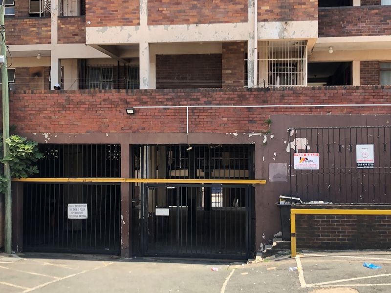 Front elevation of a brick apartment building featuring a secure gated entrance and perimeter security fencing.