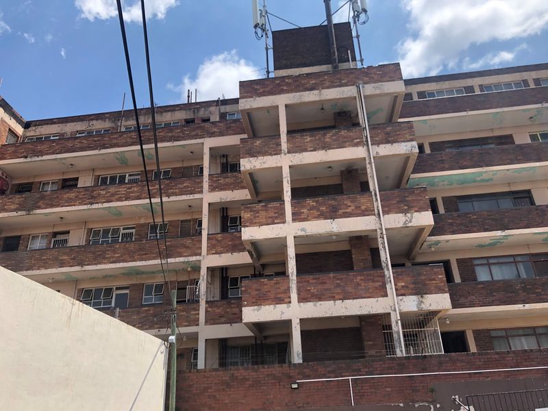 Exterior view of a multi-story brick apartment building showing balconies and signs of significant exterior wear and maintenance requirements.