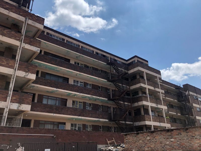 Exterior view of a multi-story brick apartment building featuring external fire escape staircases and balcony structures showing signs of weathering.