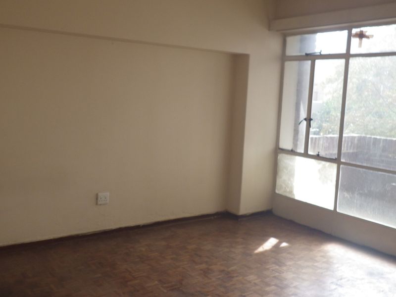 An empty living room featuring original parquet flooring and a large window providing natural light and access to an outdoor area.