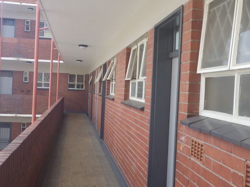 An exterior open-air walkway providing access to apartment units, featuring exposed brick walls, tiled flooring, and a metal fire escape structure.