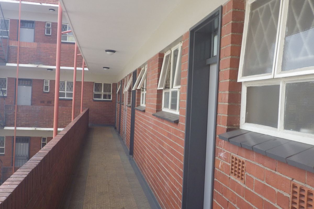An exterior open-air walkway providing access to apartment units, featuring exposed brick walls, tiled flooring, and a metal fire escape structure.