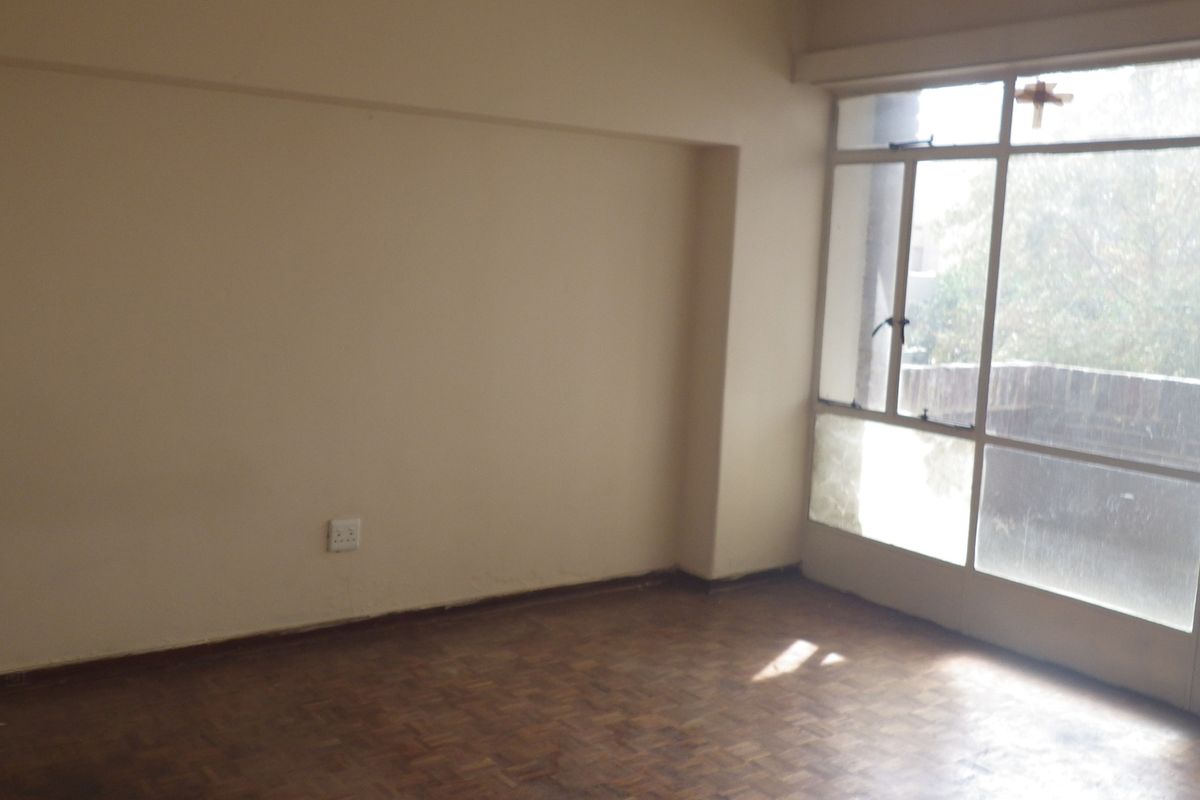 An empty living room featuring original parquet flooring and a large glass door providing natural light and access to an outdoor area.