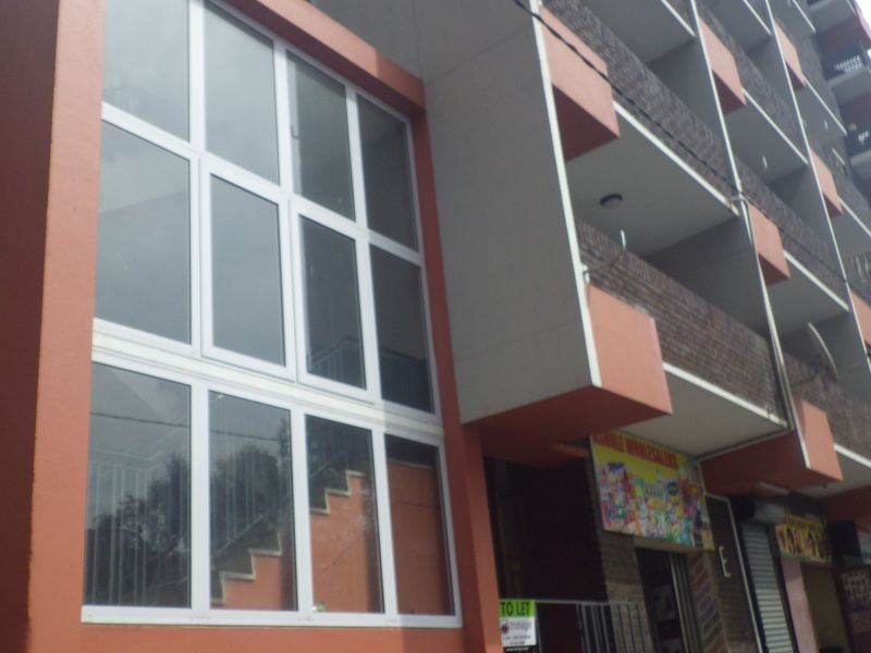 A multi-story apartment building featuring a brick facade, balconies, and ground-level commercial storefronts with large glass windows.