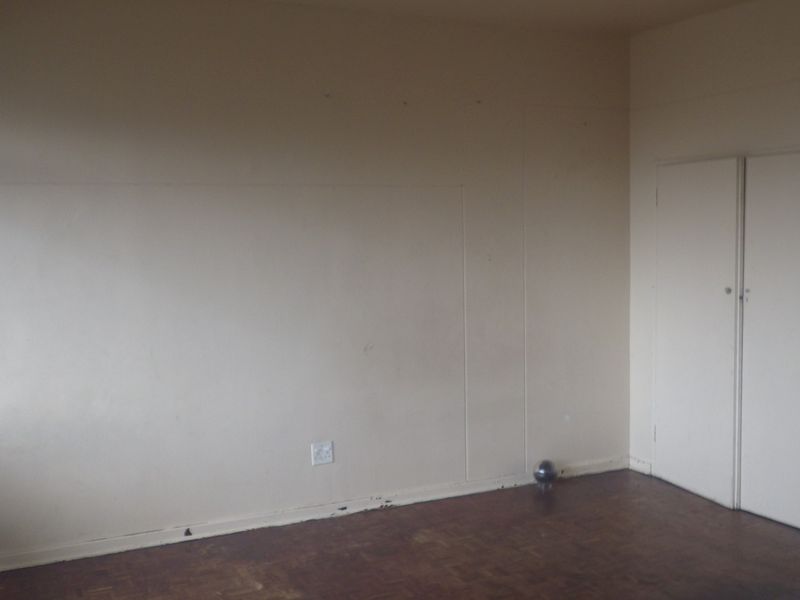 An empty bedroom featuring original parquet flooring and built-in cupboards, requiring cosmetic updates to restore its appeal.