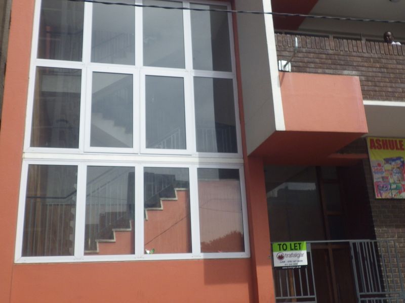 Front facade of a flat building featuring large aluminium-framed windows, brick detailing, and a secure metal entrance gate.