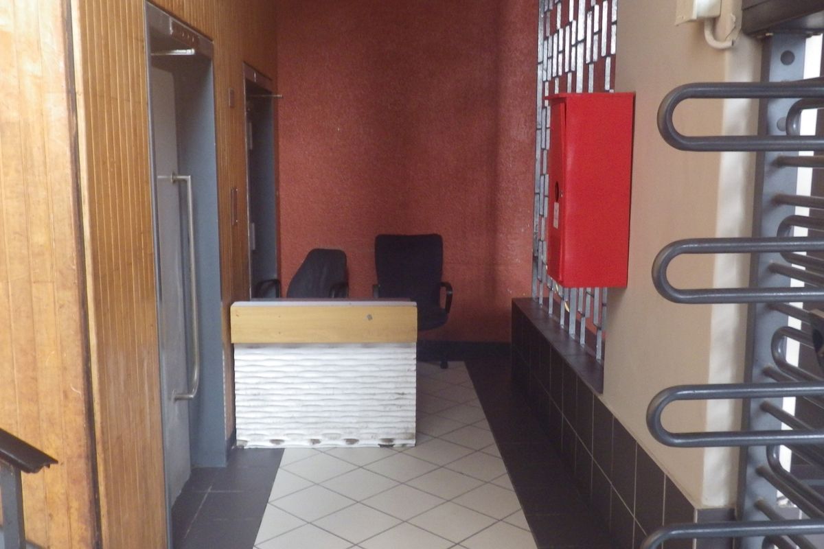 Building entrance lobby featuring an elevator, security turnstile, and reception area with tiled flooring and wood-paneled walls.
