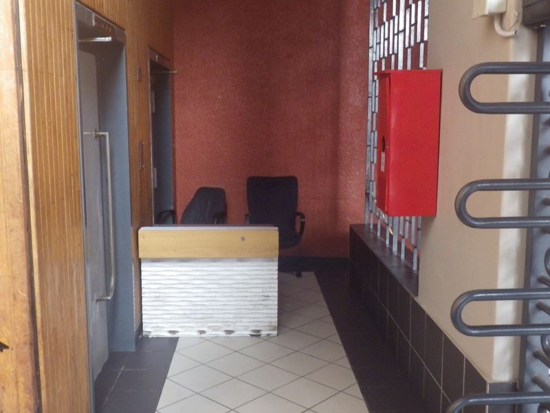 Building entrance lobby featuring an elevator, security turnstile, and reception area with tiled flooring and wood-paneled walls.