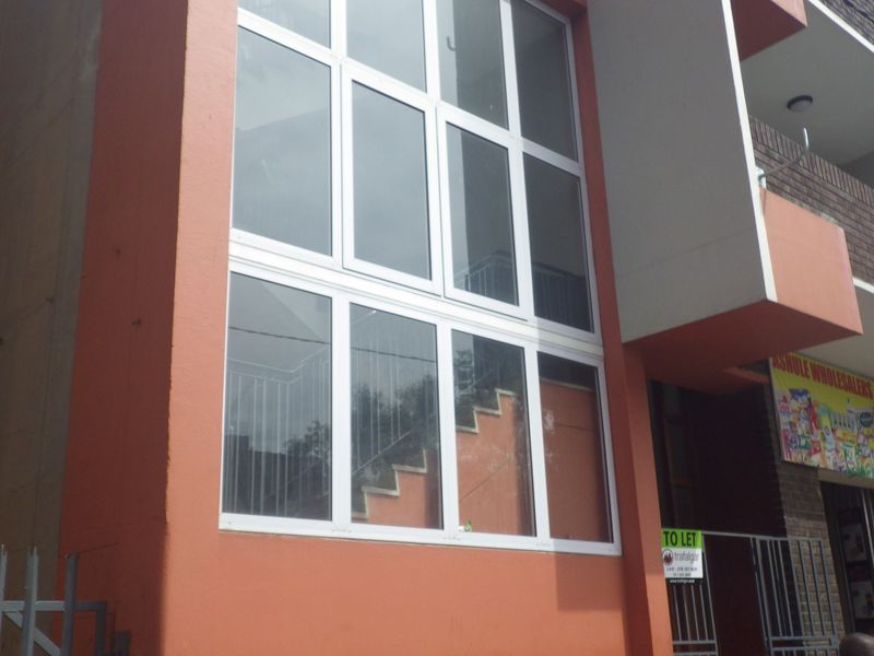 Exterior view of a flat building facade featuring a large multi-pane window, staircase, and ground-level security gate.
