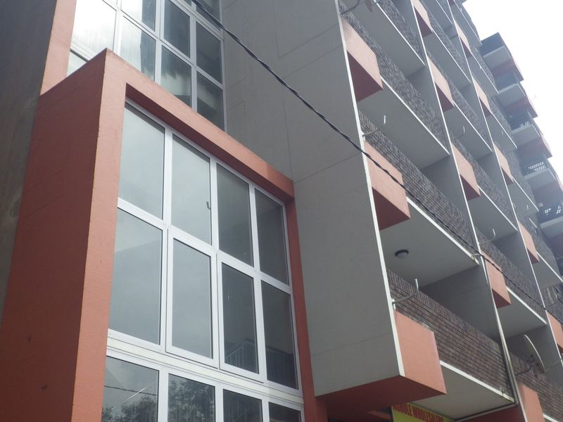 Low angle view of a multi-story apartment building facade featuring brickwork, concrete structural elements, and multiple balconies with aluminium window frames.