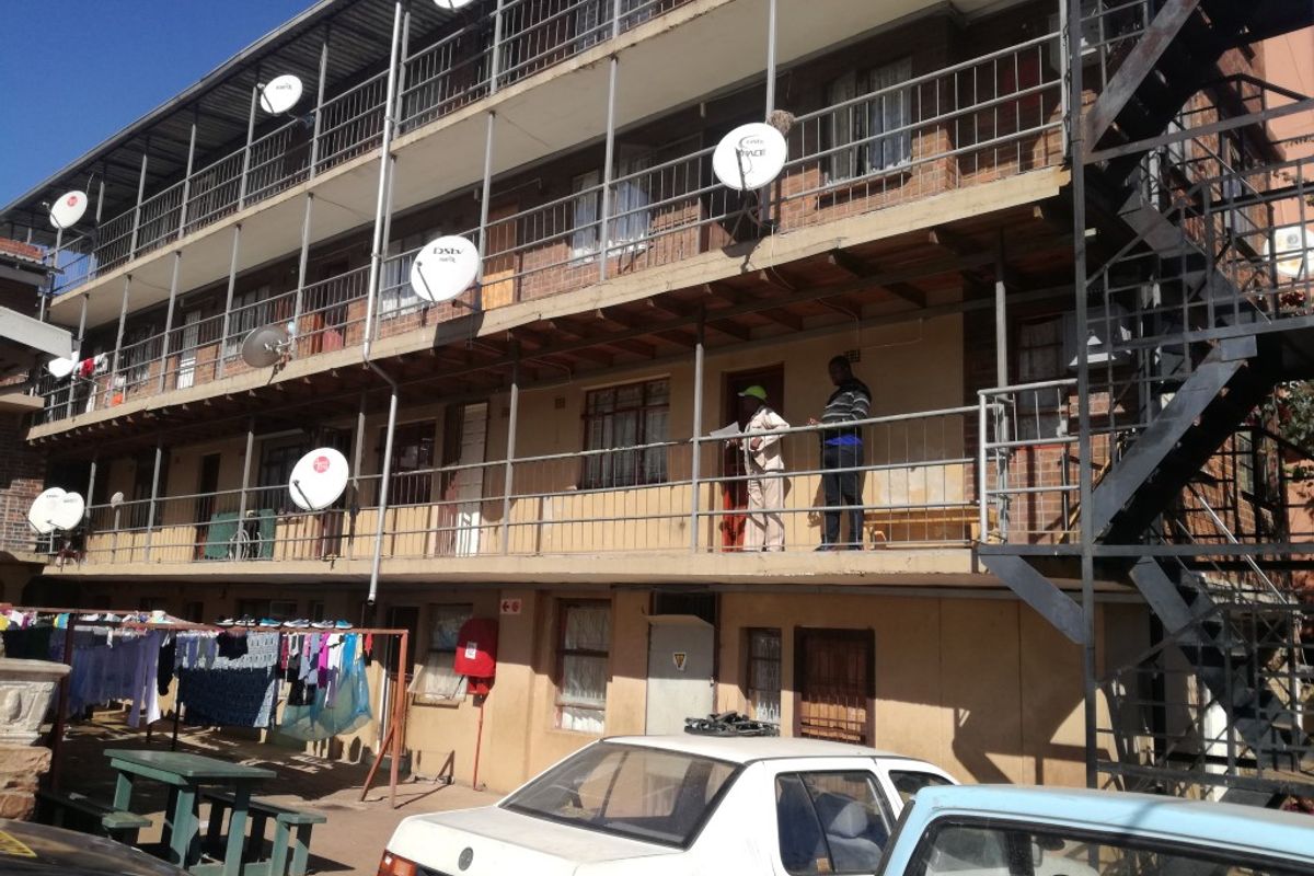Exterior view of a multi-story apartment block featuring external walkways, metal staircases, and multiple satellite dishes mounted on the building facade.