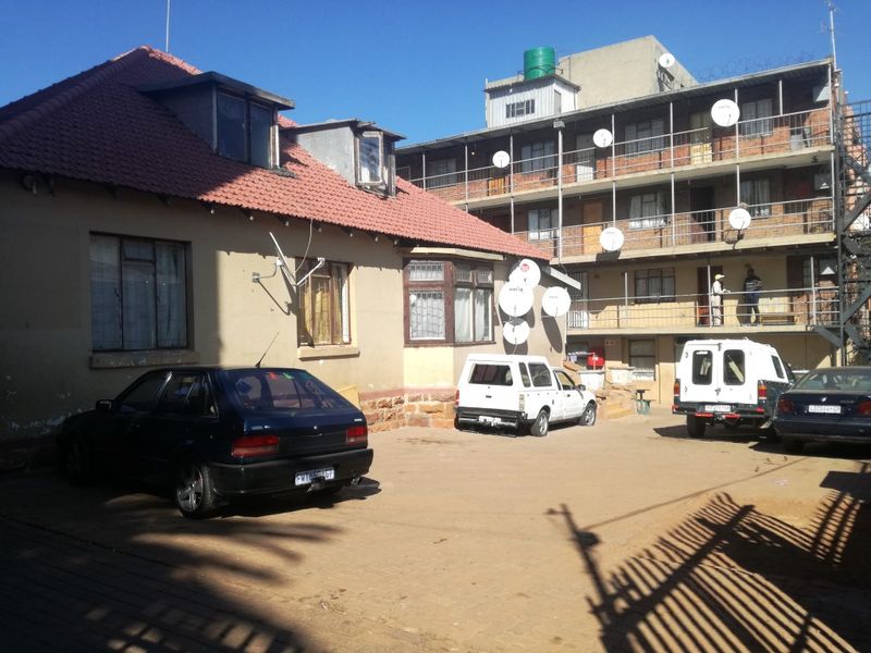 Rear view of a multi-story residential building complex featuring a tiled roof structure and shared concrete courtyard area.