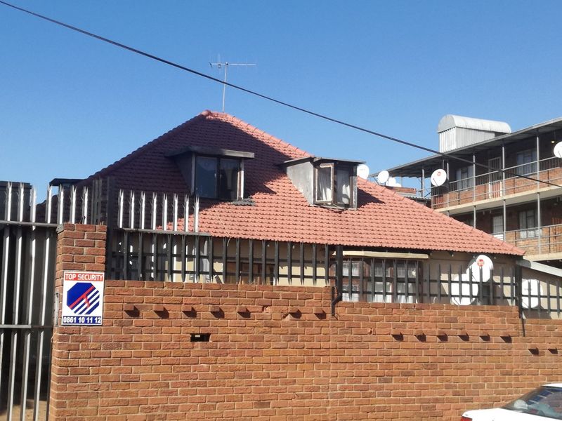 Front exterior view of a residential property featuring a brick boundary wall with security spikes and a tiled roof with dormer windows.
