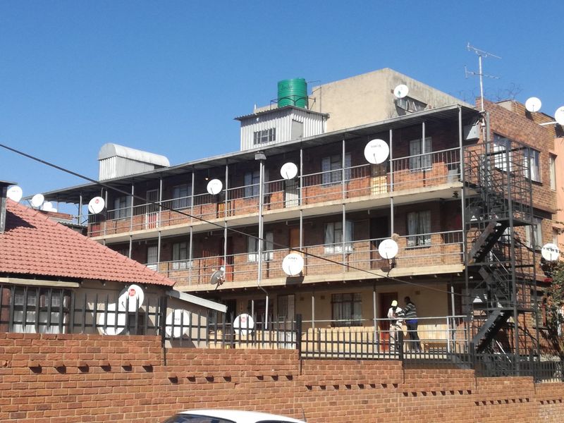 Exterior view of a multi-story brick apartment building featuring external metal staircases, balcony access, and multiple satellite dish installations.