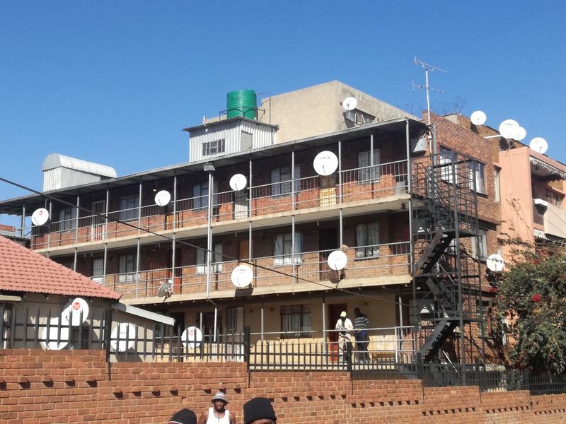 Exterior view of a multi-story brick apartment building featuring external metal staircases, balcony access, and multiple satellite dish installations.