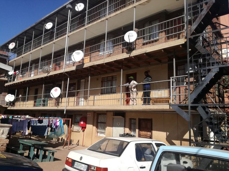 Exterior view of a multi-story apartment block featuring external walkways, metal staircases, and multiple satellite dishes mounted on the building facade.