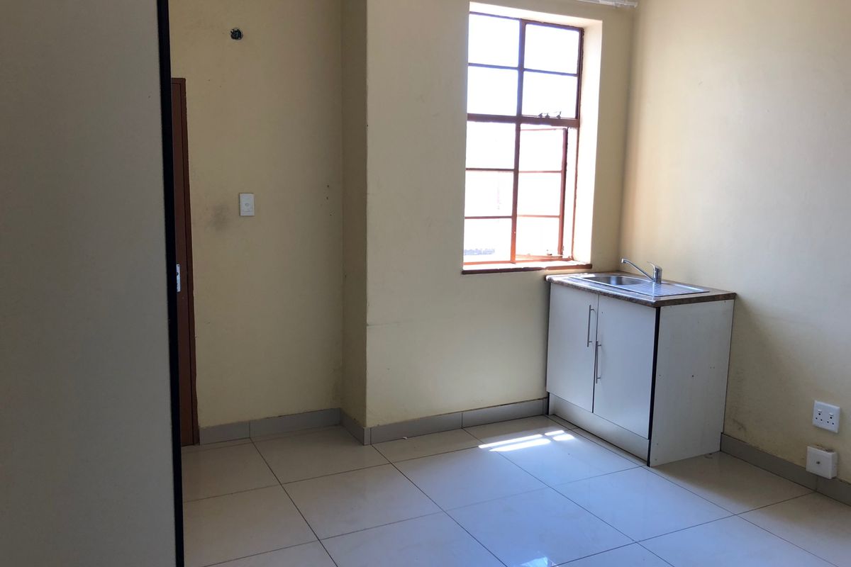 A compact kitchen area featuring tiled flooring, a single sink unit with base cabinetry, and a window providing natural light.