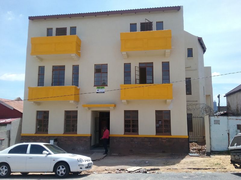 Front elevation of a multi-story apartment building featuring yellow balconies, brick base detailing, and secure entrance access.