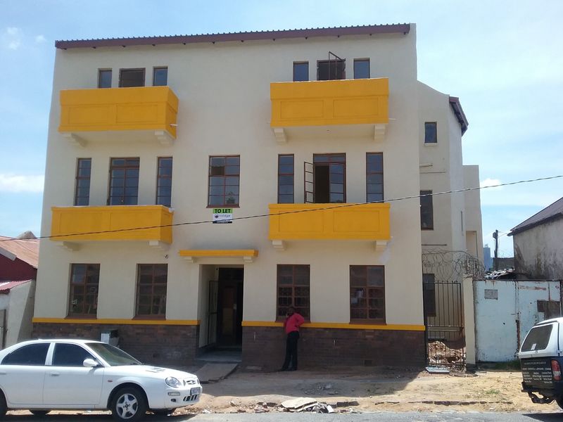 Front elevation of a multi-story apartment building featuring yellow balconies, brick base detailing, and secure gated access.