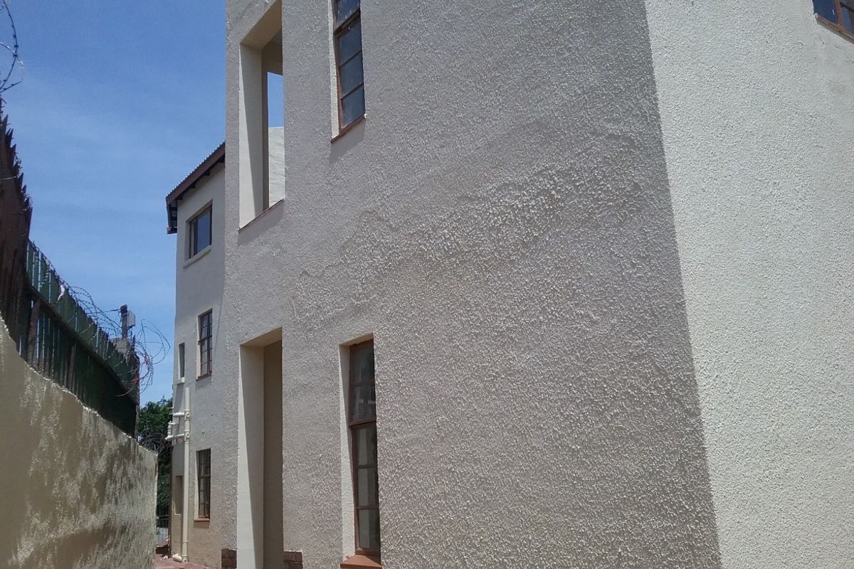 Side view of a multi-story flat building featuring textured stucco walls, casement windows, and a secure perimeter wall with razor wire.