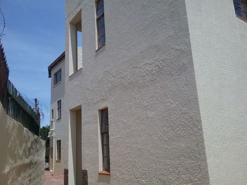 Side view of a multi-story flat building featuring textured stucco walls, casement windows, and a secure perimeter wall with razor wire.