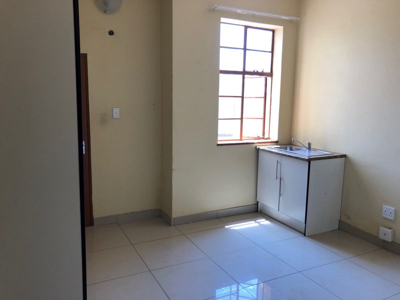 A compact, empty kitchen area featuring tiled flooring, a single base cabinet with a stainless steel sink, and a steel-framed window.
