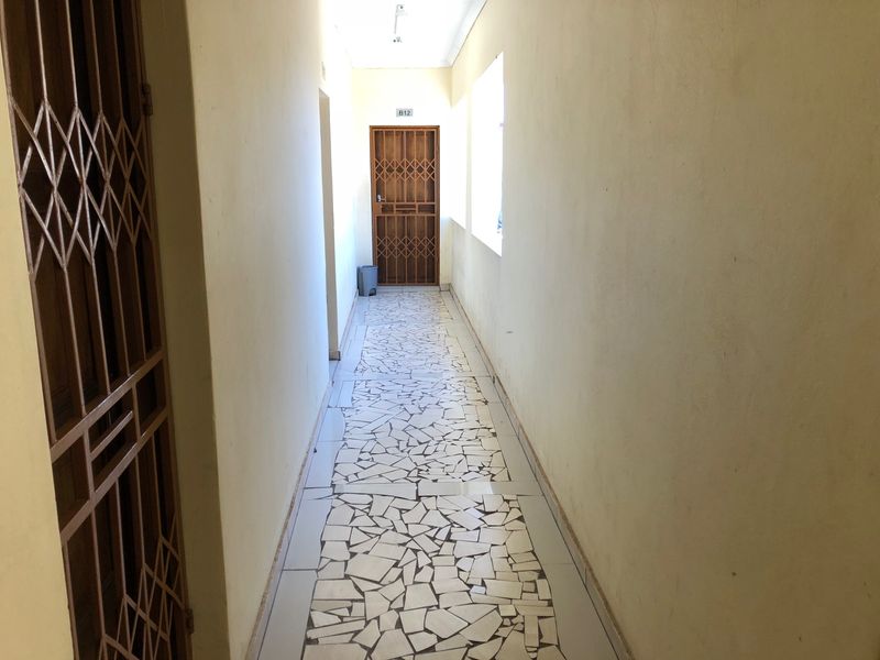 A narrow residential hallway featuring a security gate and distinctive crazy paving floor tiles, leading to a unit entrance.