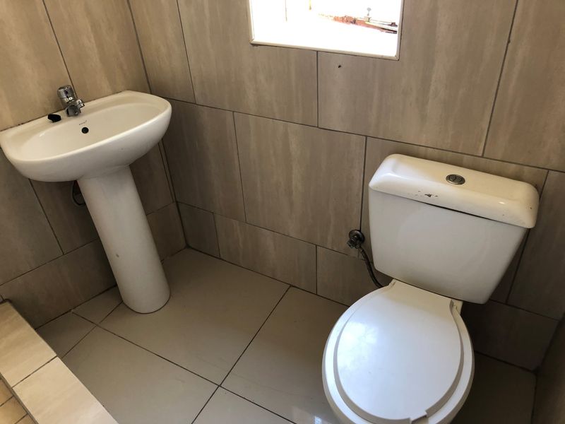 A functional bathroom featuring a pedestal basin, standard toilet, and neutral ceramic wall and floor tiling.