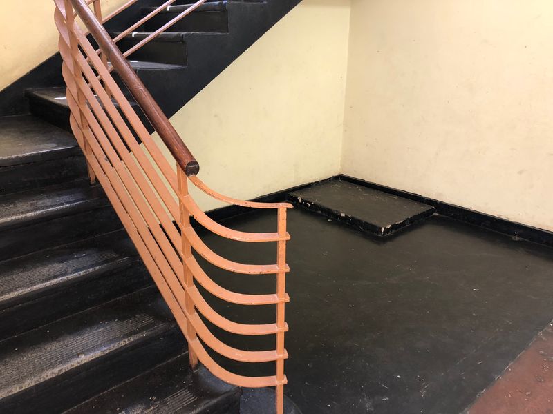 A communal staircase area featuring a metal balustrade with a wooden handrail, showing signs of wear and tear on the finishes.