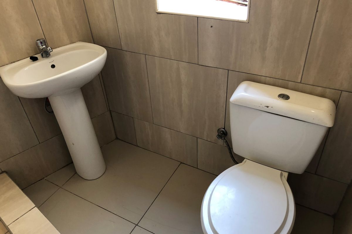 A functional bathroom featuring a pedestal basin and a standard toilet with neutral wall and floor tiling.