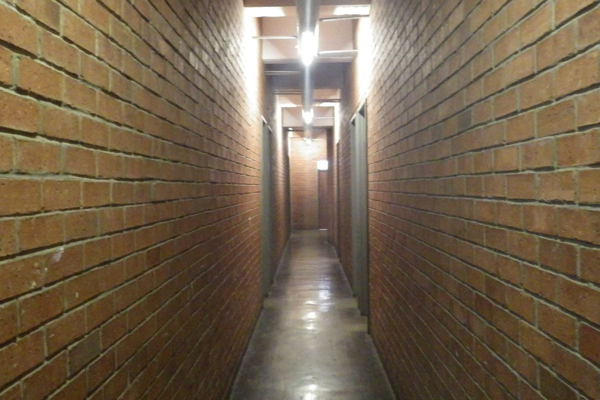 A long, narrow hallway featuring exposed brick walls, polished concrete flooring, and industrial-style track lighting.