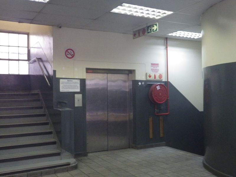 A functional building entrance area featuring a stainless steel elevator, staircase, and essential fire safety equipment including a hose reel and emergency signage.