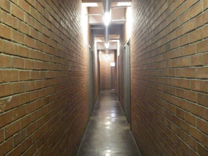A long, industrial-style hallway featuring exposed brick walls, polished concrete flooring, and overhead track lighting.