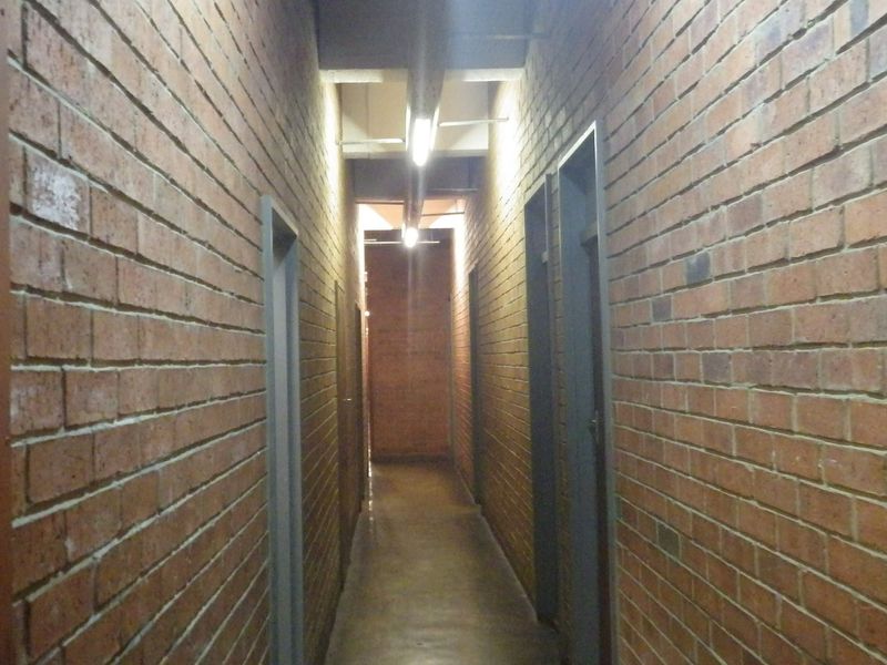 A narrow hallway featuring exposed brick walls, concrete flooring, and overhead fluorescent lighting, providing access to multiple rooms.