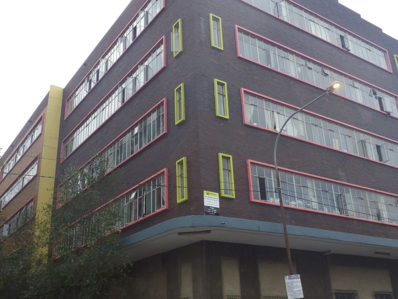 A multi-story commercial or residential building featuring a dark brick facade with distinctive colored window frames and a ground-level awning.