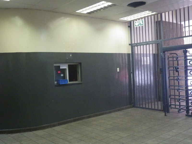 A commercial building entrance lobby featuring a security turnstile, metal security gate, reception service window, and tiled flooring.
