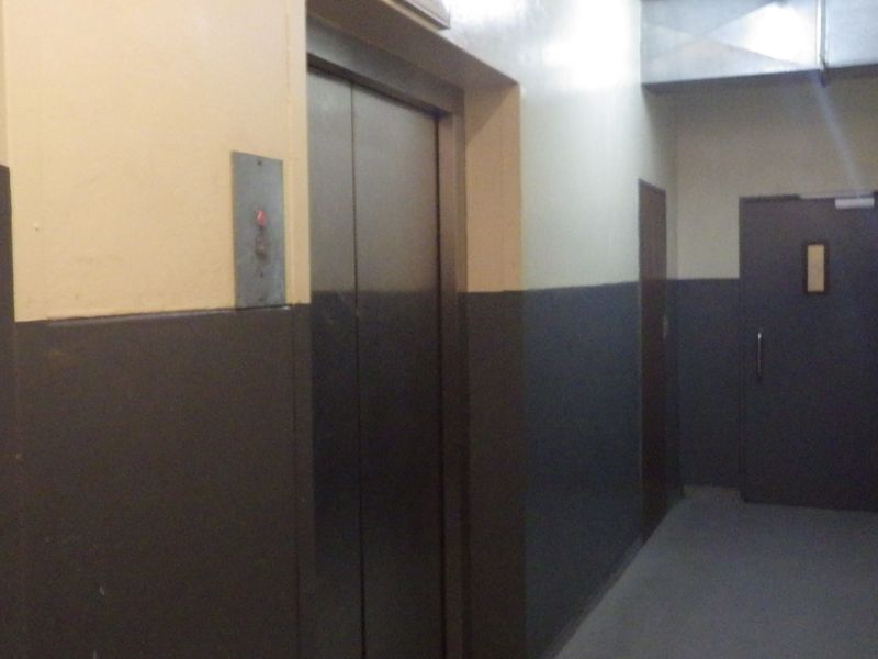 A utilitarian hallway featuring a metal elevator door, a fire-rated door, and exposed ventilation ducting, showing signs of wear on the walls.