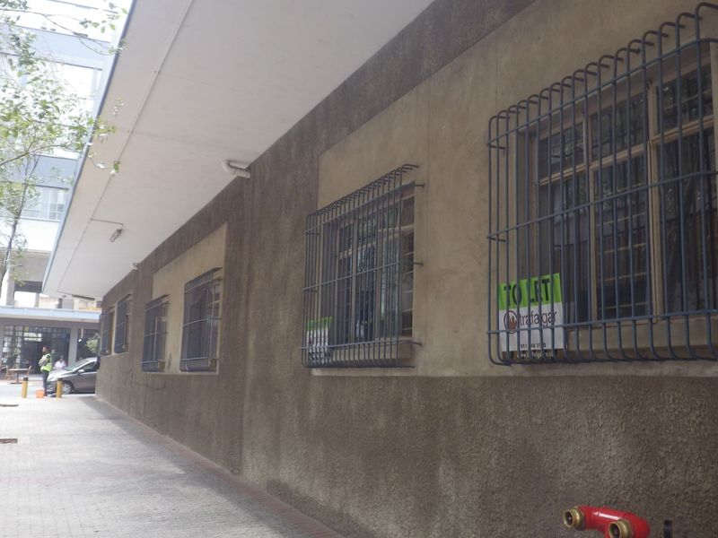 Exterior view of a building facade featuring security-barred windows, a paved walkway, and a fire hydrant connection.