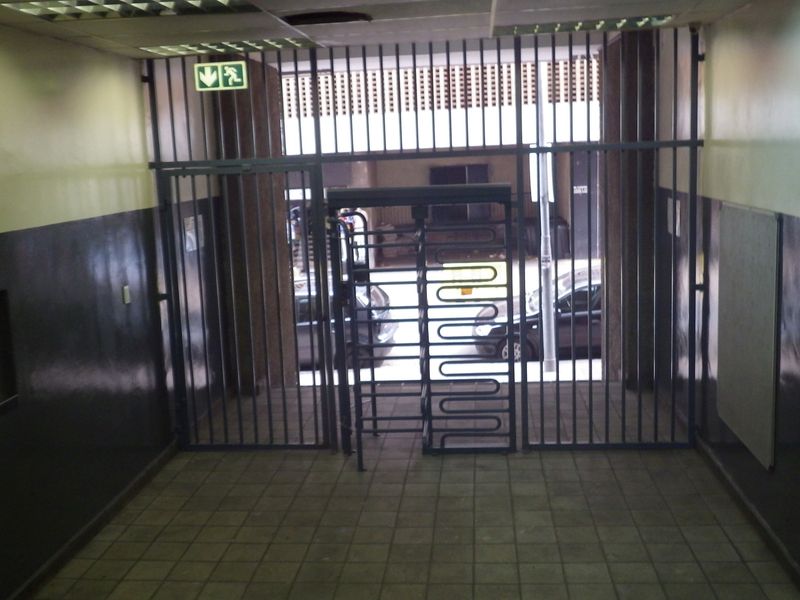 A secure building entrance lobby featuring a metal turnstile, security gates, tiled flooring, and a drop ceiling.