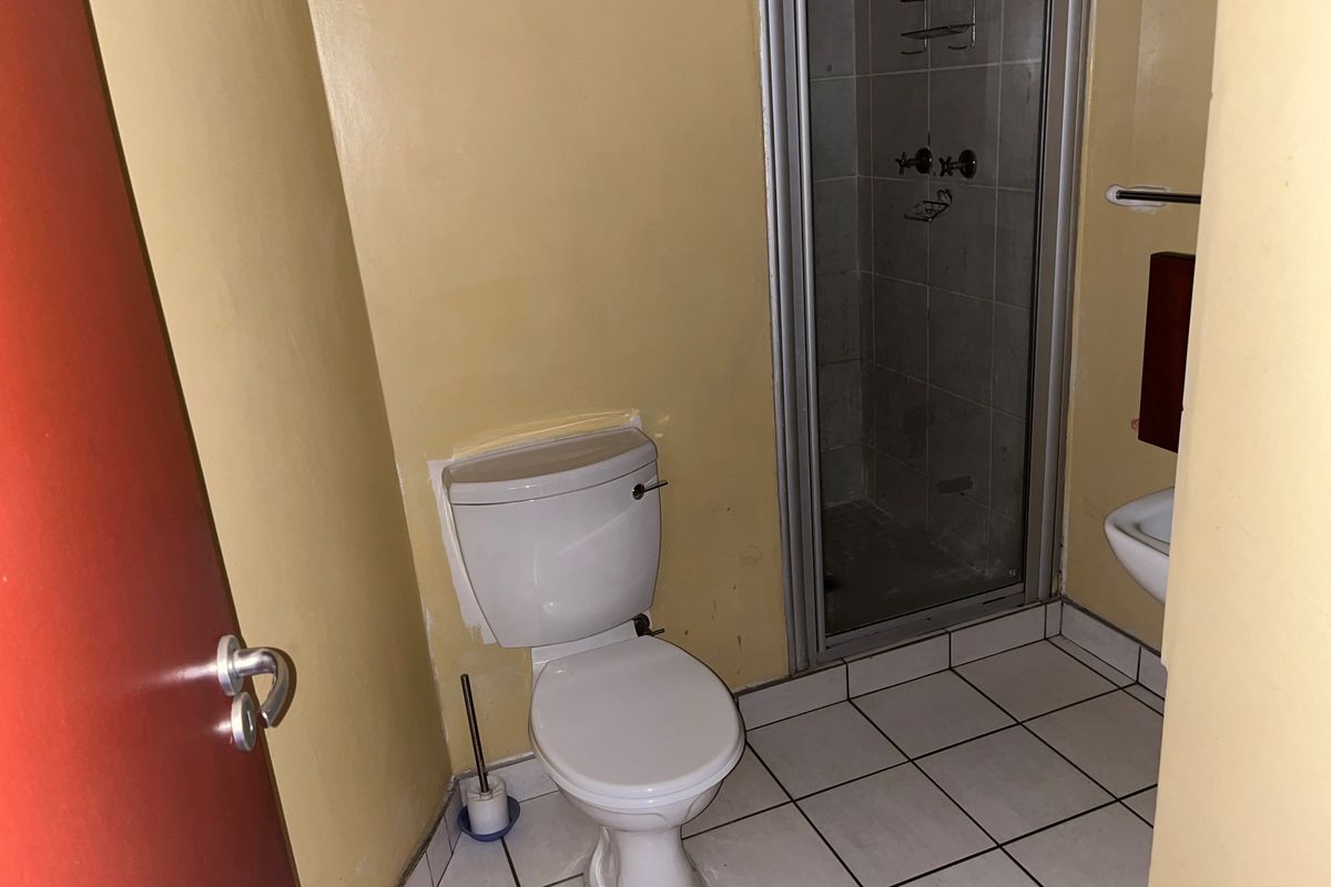 A compact bathroom featuring a white toilet, a tiled shower enclosure with a glass door, and tiled flooring.
