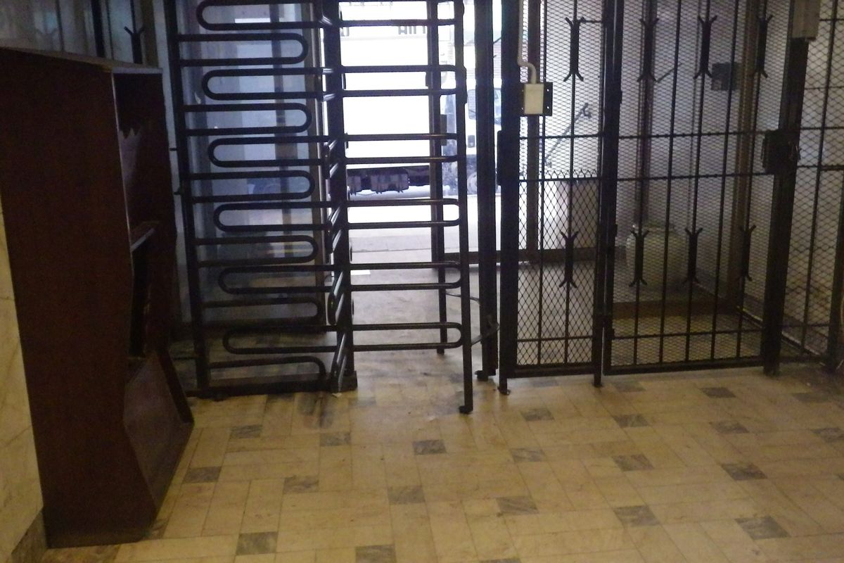 Building entrance lobby featuring security turnstiles, metal security gates, and tiled flooring with marble wall accents.