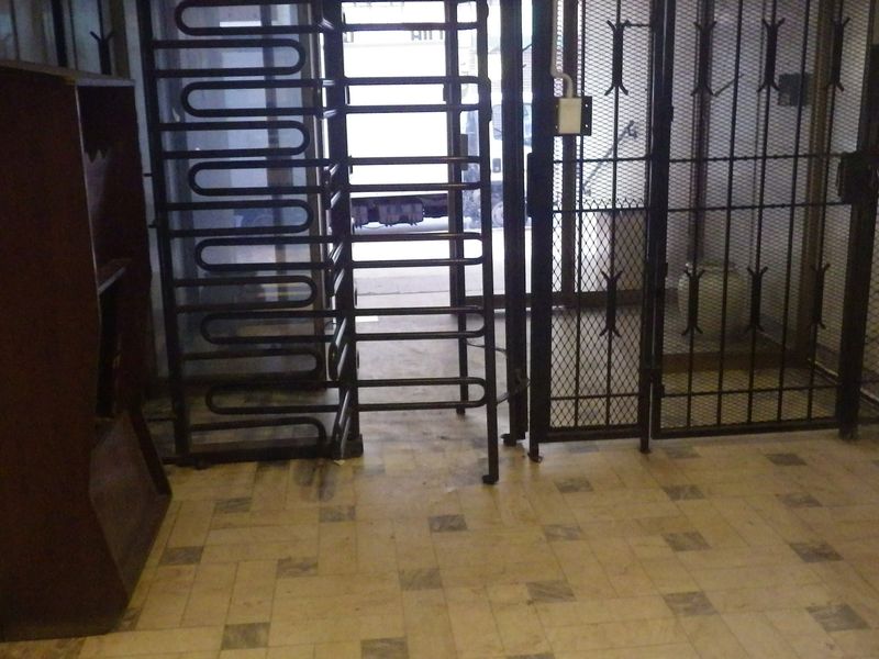 Building entrance lobby featuring security turnstiles, metal security gates, and tiled flooring with marble wall accents.