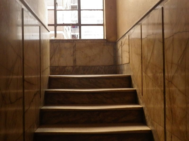 A stairwell featuring vintage marble wall cladding and a steel-framed window, showing signs of age and wear.