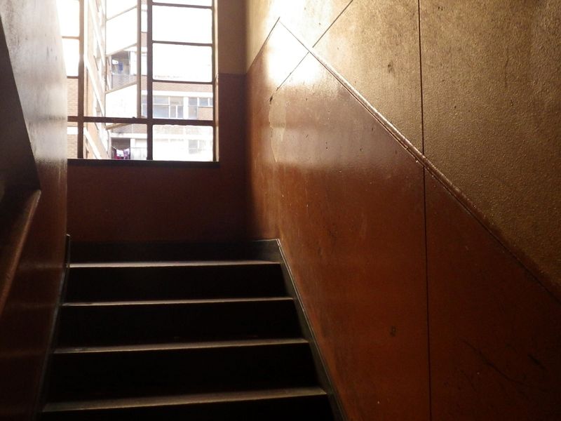 A communal stairwell area featuring a steel-framed window and painted wall finishes showing signs of wear.
