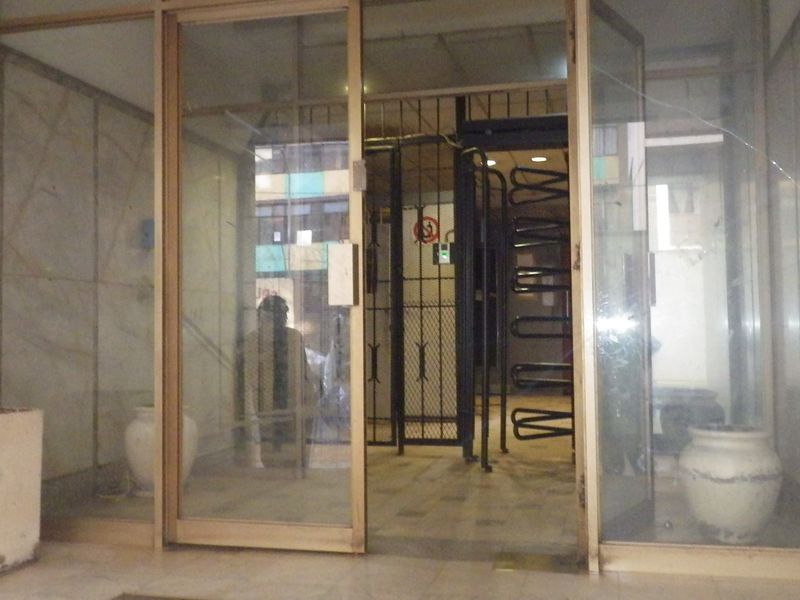 Building entrance lobby featuring glass sliding doors, metal turnstile security access, and stone wall cladding in need of maintenance.