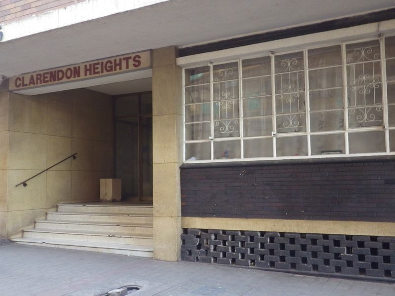 Front entrance view of Clarendon Heights apartment building featuring brick facade, security window bars, and concrete access steps.