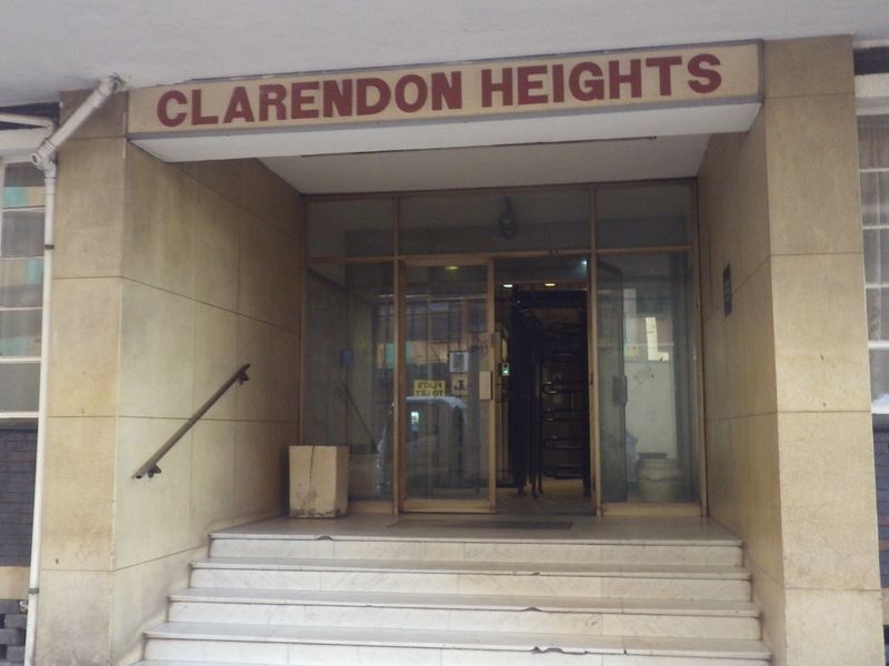 The front entrance of Clarendon Heights featuring stone cladding, a glass door, and concrete steps leading to the building lobby.